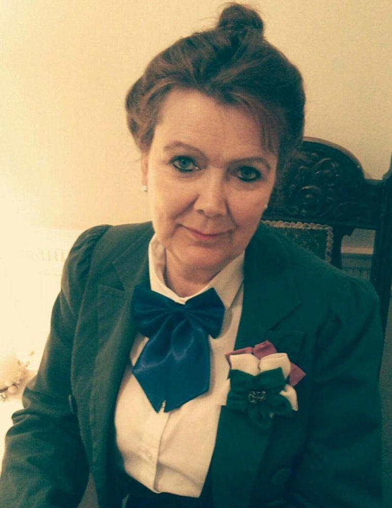 Photo of Glenys Horton sat in a green suit with hair up.